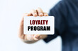 Loyalty program text on blank business card being held by a woman's hand with blurred background. Business concept about loyalty program.