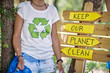 Woman with plastic bag for picking up trash, standing in front of wooden board saying, Keep our planet clean. Volunteers in nature picking up trash. Environmentalism, green, lifestyle concept.