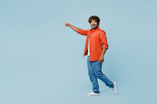 Full Body Smiling Young Indian Man Wear Orange Red Shirt White T-shirt Walk Go Point Index Finger Aside On Area Isolated On Plain Pastel Light Blue Cyan Background Studio Portrait. Lifestyle Concept.