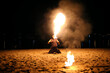 Man fire juggler performing at night on a sandy beach
