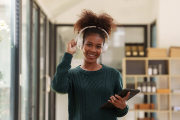 Wall Mural - Happy woman in headphones holding tablet with fist raised excited about success.