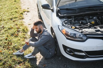 Man use a cellphone call garage in front of the open hood of a broken car on the road in the forest. Car breakdown concept.