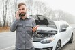 © Serhii - Sad driver calling car service, opening hood, having engine problem standing near broken car on the road. Car breakdown concept
