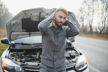 Wall Mural - A young man near a broken car with an open hood on the roadside.