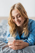 © LIGHTFIELD STUDIOS - cheerful woman messaging on smartphone while lying in blue pajama on bed.