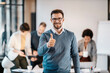 © Dusan Petkovic - Portrait of a happy businessman giving thumbs up at the camera while his colleagues working in a blurry background at the office.