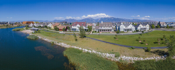 Wall Mural - Aerial panorama view of lakefront single-family houses at Daybreak, Utah. There is a lake at the front with grass and pathway on its shore near the houses against the mountains and blue sky.