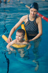 Happy little boy learning to swim with pool noodle