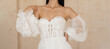 Beautiful bride dressed in a white wedding dress with a deep neckline. Beautiful corset with floral lace and fancy long lantern sleeves. Wedding details. Slim female model.