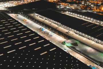 Wall Mural - Aerial view of a warehouse of goods at night. Aerial view of the logistics center. Brightly lit trailers and trucks in a warehouse parking lot