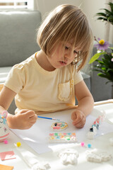 Wall Mural - A cute little girl is sitting at a table and doing Easter crafts, coloring Easter figurines. Creativity and hobbies.