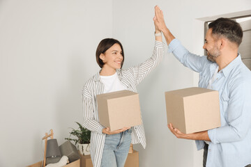 Canvas Print - Happy couple with moving boxes giving high five in new apartment