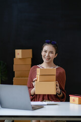 Wall Mural - Asian female business owner uses laptops and tablets to take and verify online orders to prepare boxes. Packing products for delivery to customers, SME business concept, e-commerce, online shopping ve