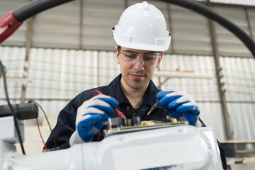 Male electrician worker checking, repair, maintenance operation electric system of robotic arm in factory. Male electrician using electrical meters working with operation electric system of robot arm