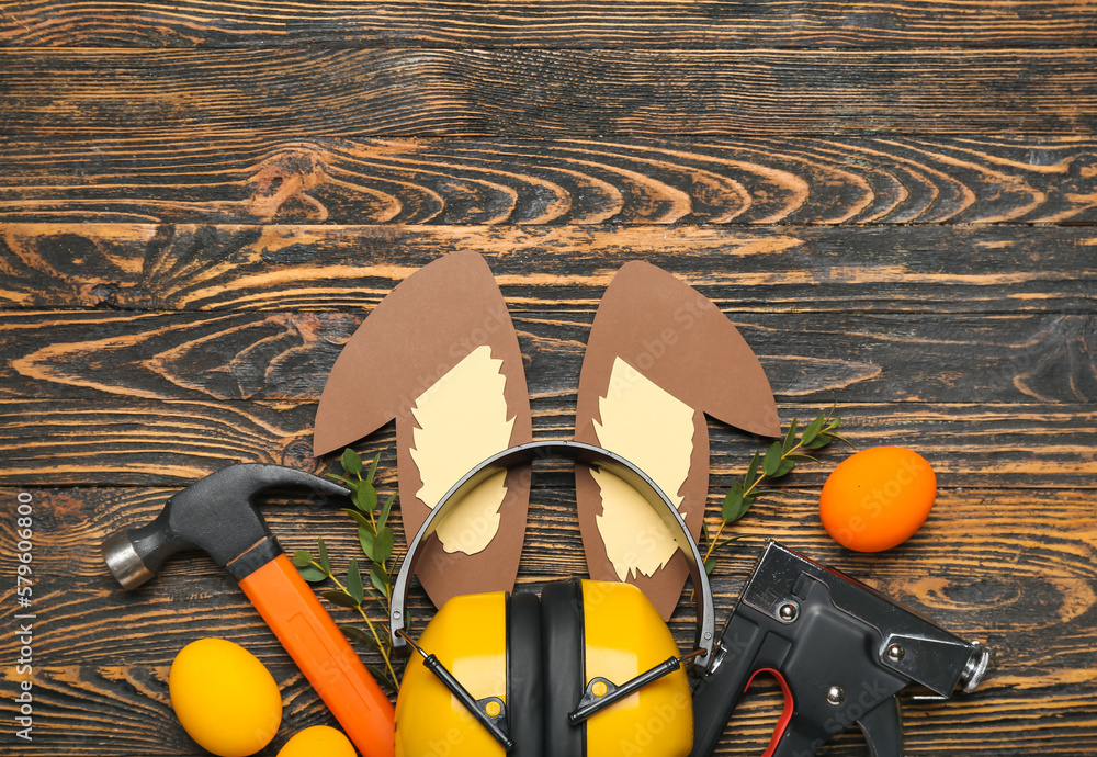 Construction tools with paper bunny ears, Easter eggs and eucalyptus on dark wooden background