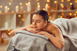 Woman enjoying beauty procedures at a modern spa salon. Happy, relaxed young girl with closed eyes lying on the bed, with beautiful lights gleaming in the background. Spa day, beauty, pleasure concept