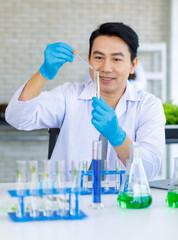 Wall Mural - Asian professional male scientist researcher in white lab coat and rubber gloves sitting holding dropper dropping reagent into sprout seedling vegetable sample in test tube on laboratory table