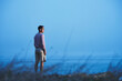 © Cavan Images - Rear view of man looking away while standing at beach against clear blue sky at dusk