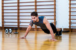 © Cavan Images - Full length of muscular athlete doing push-ups on hardwood floor in gym