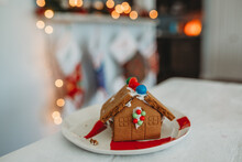Gingerbread House With Twinkle Lights And Stocking Blurred In Background