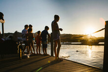 Group Of Kids Stand On Dock By Lake In Summer Sunshine And Feed Fish