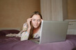 © GRON777 - A young woman in a country house, works on a laptop, lies on a bed, watches online entertainment, she has a headache, eye fatigue. Technology concept, fatigue.Suffers from dizziness, overworked