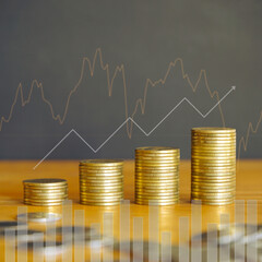 Stack of golden money coin on wood desk with graph and up arrow. Financial background concept.