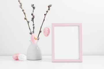 Wall Mural - Easter holiday composition. Empty pink photo frame mockup, vase with willow branches, easter eggs, bunny on white table background. Minimal conceptEaster. Front view