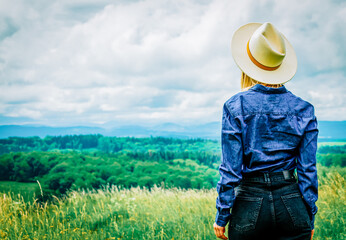 Canvas Print - Blonde cowgirl in hat at meadow with mountains on background