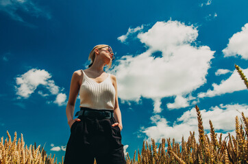 stylish woman with blond hair posing in formal clothes in wheat field