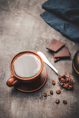 Wall Mural - Black coffee drink in a clay cup, chocolate pieces and coffee beans in a spoon on dark background