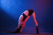 © standret - Bends to the leg, stretching. Beautiful muscular woman is indoors in the studio with neon lighting