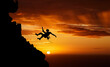 Sunset sky abseiling, mountain silhouette and hiking man hanging on shadow rope. Fitness risk, adventure freedom challenge and strong, surreal nature adrenaline and cliff climbing on orange landscape