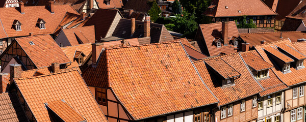 Scenic panoramic view traditional shingle tiled red rooftop old ancient medieval european german small town Quedlinburg church against blue sky background. Unesco heritage list travel destination