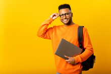 Smart Inteligente Indian Male Employee Or Freelancer Man Holding Laptop And Looking At Camera With Happy Smile, Isolated On Yellow Background, Arab Student With Backpack Adjusting His Glasses