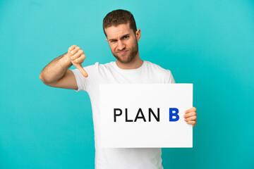 Wall Mural - Handsome blonde man over isolated blue background holding a placard with the message PLAN B and doing bad signal