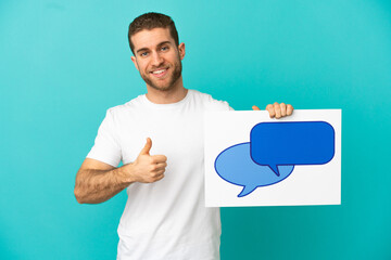 Wall Mural - Handsome blonde man over isolated blue background holding a placard with speech bubble icon with thumb up