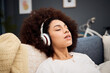 © D Lahoud/peopleimages.com - Music, relax and black woman on a sofa listening to radio, streaming or wellness podcast in a living room. Headphones, woman and rest on a couch with online audio track, meditation and playlist