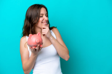 Poster - Young Caucasian woman holding a piggybank isolated on blue bakcground thinking an idea and looking side