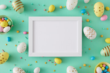 Wall Mural - Easter celebration concept. Flat lay photo of white photo frame colorful easter eggs dragees and sprinkles on turquoise background