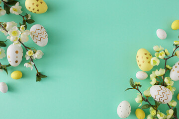Wall Mural - Easter decoration concept. Top view photo of yellow white easter eggs and cherry blossom branches on turquoise background with copyspace