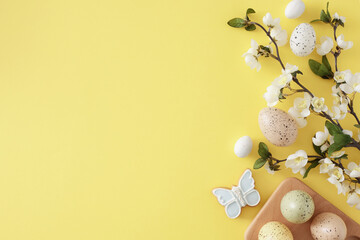 Wall Mural - Easter celebration idea. Top view photo of colorful easter eggs in wooden holder and spring blossom branch on isolated yellow background with empty space