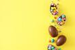 Easter sweets idea. Top view photo of chocolate eggs with сolorful dragees and sprinkles on isolated yellow background with empty space. Easter concept
