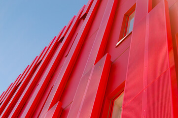 Modern red architectural office building. Metal sheets covering the exterior of the structure. Modern futuristic style building. Clear sky at the background. Unique building.