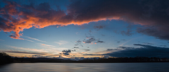 panoramic sunset sky on pond with distant hill and tree silhouette. early spring czech landscape, bl