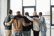 © LIGHTFIELD STUDIOS - Back view of interracial group of anonymous alcoholics hugging during meeting in rehab center.
