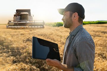 Fototapete - Farmer with digital tablet stands next to combine harvester. Smart farming concept.	