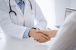 © rogerphoto - Doctor and patient shaking hands while sitting opposite of each other at the table in clinic, just hands close up. Medicine concept.