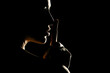 Silhouette of unknown woman with the face in the shadow holding finger on her lips on a black background