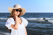 © rogerphoto - Happy blonde woman is posing on the ocean beach with sunglasses and a hat. Evening sun.